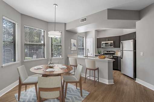 A dining room with a table set for four and a kitchen in the background.