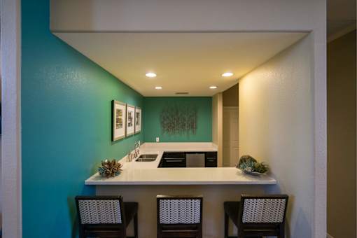 A kitchen with a white counter top and chairs.