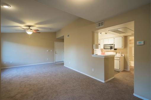 A room with a ceiling fan and a kitchenette in the background.