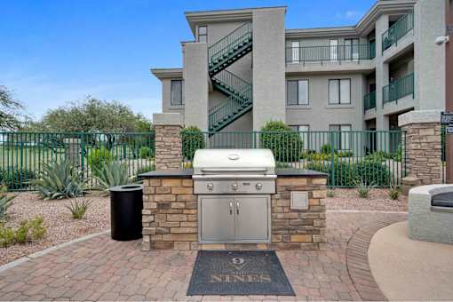an outdoor kitchen with a grill and a trash can in front of an apartment building