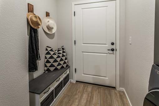 A white door is in a hallway with a bench and a hat hanging on the wall.