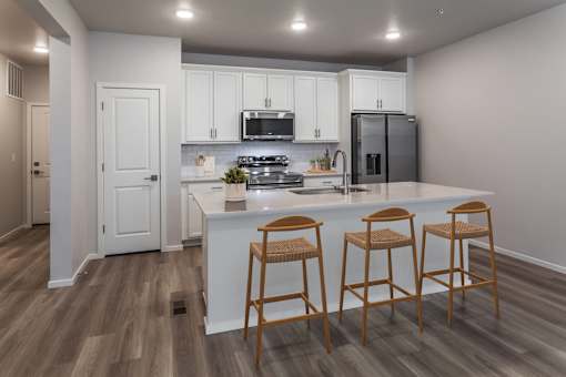 A kitchen with white cabinets and a bar area with three stools.