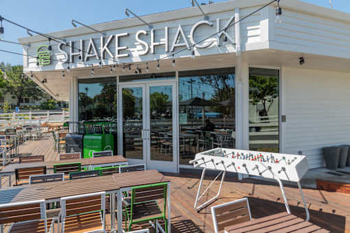 A Shake Shack restaurant with a green trash can and a white table.