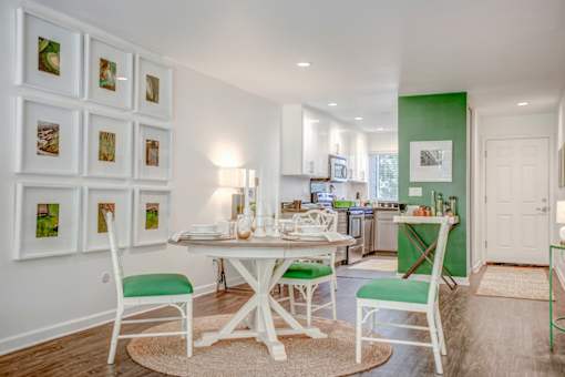 A white dining table with green chairs and pictures on the wall.
