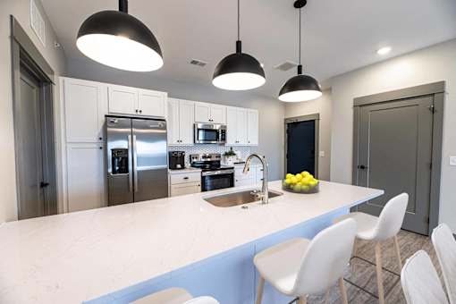 A modern kitchen with a large island and white chairs.