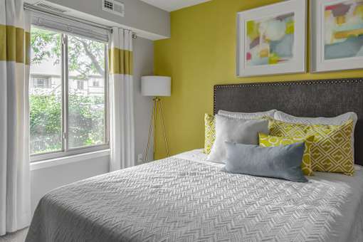 A bedroom with a bed, pillows, a lamp, and two paintings on the wall.