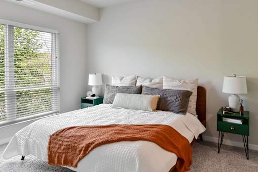 A bedroom with a large bed and a window with blinds.