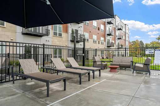 A patio with a black umbrella and a bench.