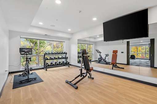 A spacious home gym with a variety of exercise equipment and a flat-screen TV mounted on the wall.