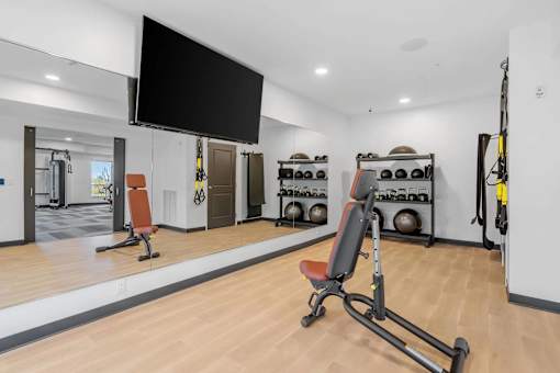 A gym with a variety of equipment including a bench, weights, and a television.