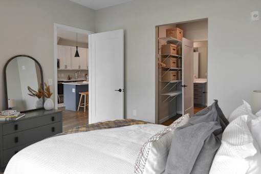 A bedroom with a white bed and a mirror on the dresser.