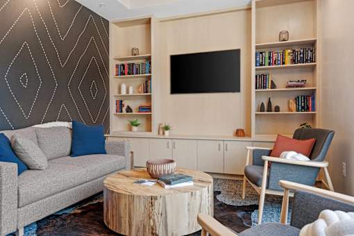 A living room with a grey couch, a wooden coffee table, a chair, a TV, and a bookshelf.