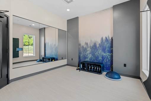 A room with a large painting of a forest on the wall and a blue ottoman.