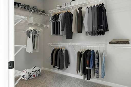 A white closet with clothes hanging on shelves and a Converse bag on the floor.