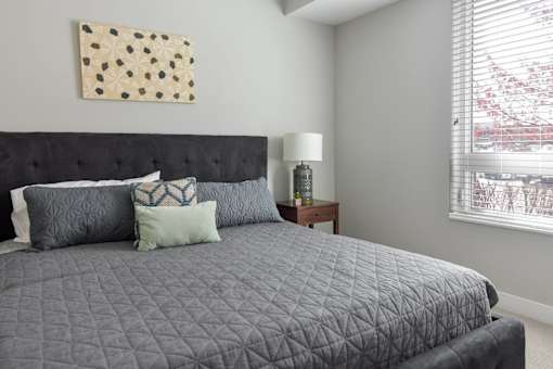 A bed with a black headboard and grey comforter with four pillows on it.