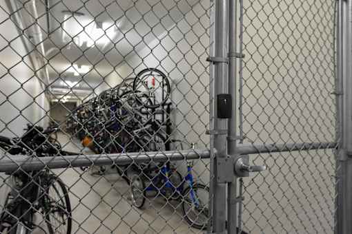 A chain link fence with a gate is in front of a wall with a bunch of bicycles hanging on it.