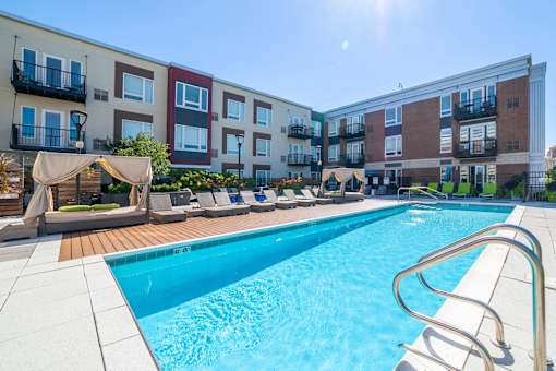 A swimming pool surrounded by lounge chairs and umbrellas in front of apartment buildings.
