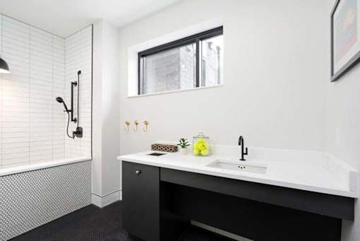 A bathroom with a black and white theme featuring a sink, a mirror, and a shower.