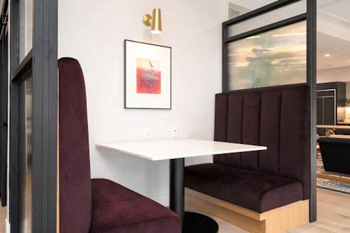 A white table with a red chair and a framed picture of a drink on the wall.