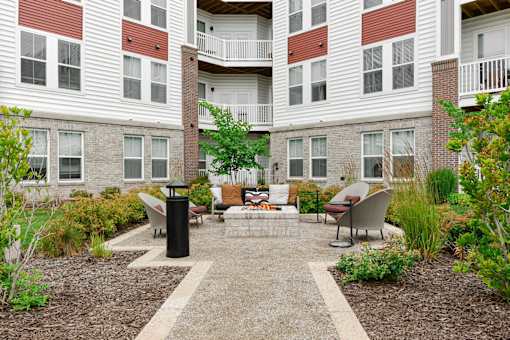 A courtyard with a black trash can and a bench with a cushion on it.
