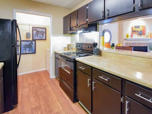 A kitchen with a black refrigerator and brown cabinets.
