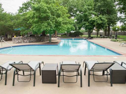 A pool surrounded by trees and chairs.