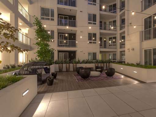 A modern courtyard with a tree, chairs, and a table surrounded by apartment buildings.