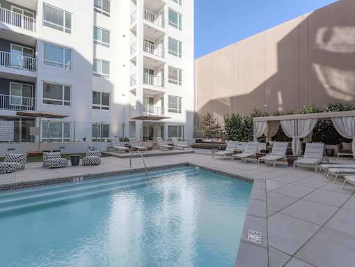 A large swimming pool is surrounded by lounge chairs and umbrellas in a courtyard.
