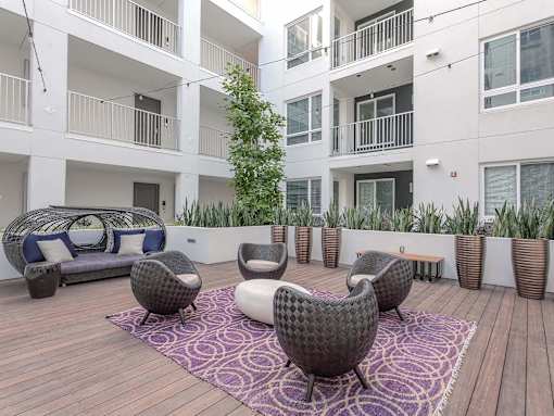 A patio with a couch, chairs, and a tree.