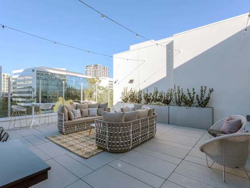 A patio with a white couch and a table with a glass top.