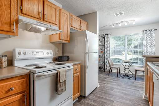 A kitchen with a white stove and refrigerator, wooden cabinets, and a dining table with chairs.