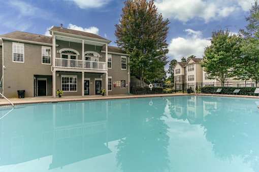 A large swimming pool in front of a two-story building with a balcony.