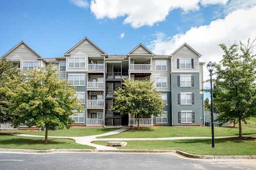 A large apartment complex with multiple balconies and trees in front.