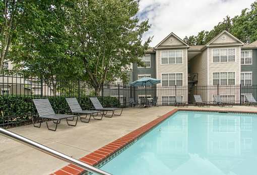 A swimming pool in front of a building with a fence and trees.