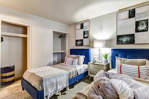 A bedroom with two beds and a nightstand with a lamp.