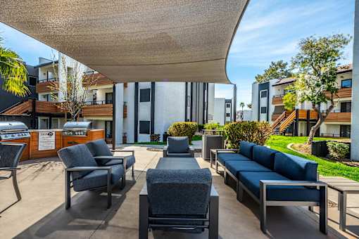 A patio with a black couch and chairs under a white awning.
