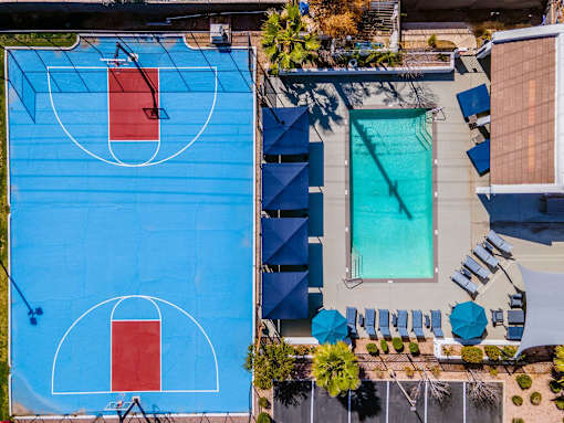 A basketball court is surrounded by a pool and lounge chairs.