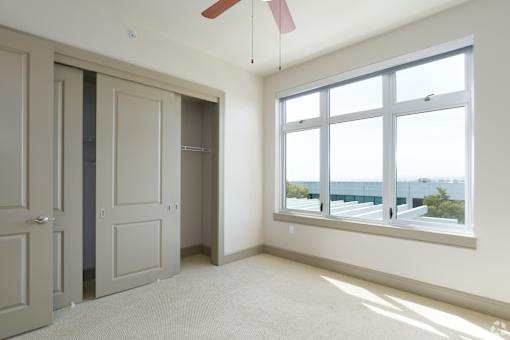 A room with a window overlooking the city and a ceiling fan.