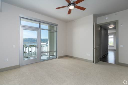 A room with a ceiling fan and a large window overlooking a balcony.