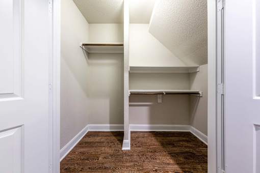 A white closet with a shelving unit and a wooden floor.