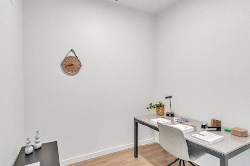 A white desk with a plant and a clock on the wall.