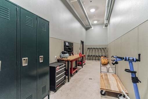 A workshop with green lockers, a workbench, and a cart with a bag on it.