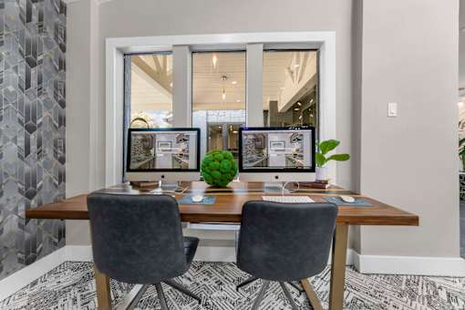 A modern home office with a wooden desk, two chairs, and two computer monitors.