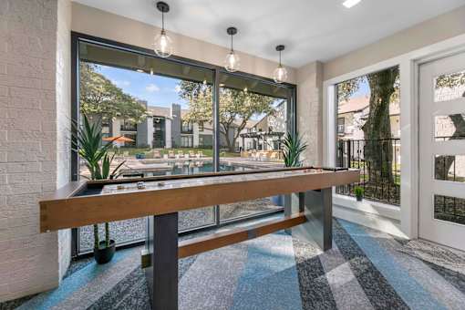 A long wooden bench is in front of a window with a view of a garden.