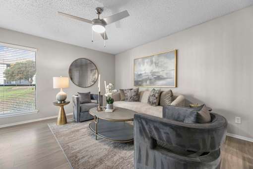 A living room with a grey couch, a round mirror, and a painting on the wall.