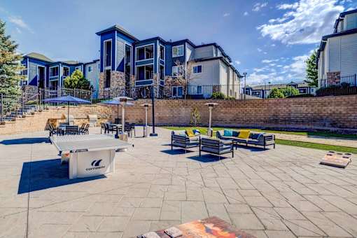 A playground with a ping pong table and benches is surrounded by a brick wall and apartment buildings.