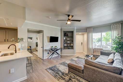 A modern living room with a brown couch and a white kitchen area.