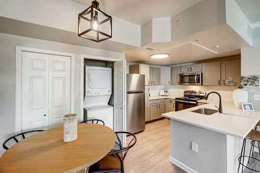 A kitchen with a table and chairs in the foreground and a refrigerator, microwave, and oven in the background.