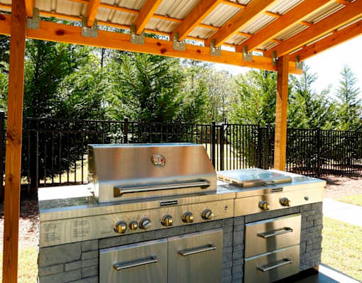 A stainless steel outdoor grill with a wooden pergola above it.
