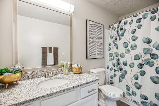 A bathroom with a sink, toilet, and a shower curtain with leaf patterns.